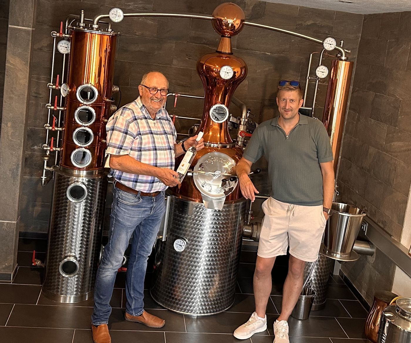 Brennmeister Bernhard Zender mit einer Flasche Nelchesbirne und sein Sohn Andreas an der kupfernen Brennanlage der Eifelbrennerei Bernhard Zender in Wolsfeld