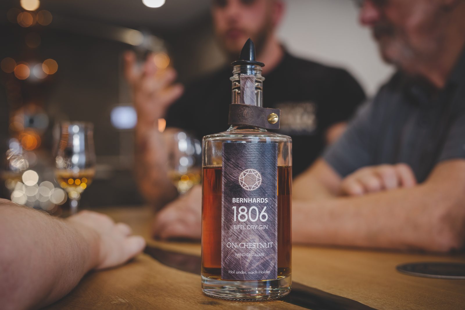 Flasche Bernhards 1806 On Chestnut auf dem Tresen, im Hintergrund eine Verkostung mit gefüllten Gläsern